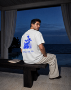 White | Lifestyle | Man on a dark wooden bench by a pool at dusk wearing the Well Read Tee in White, an open book beside him